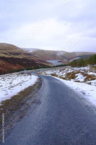 frozen road in Scottish hills covered in a little snow and a frozen dam