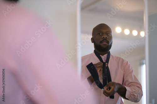 African American man in shirt dressing up and adjusting tie on neck at home. photo