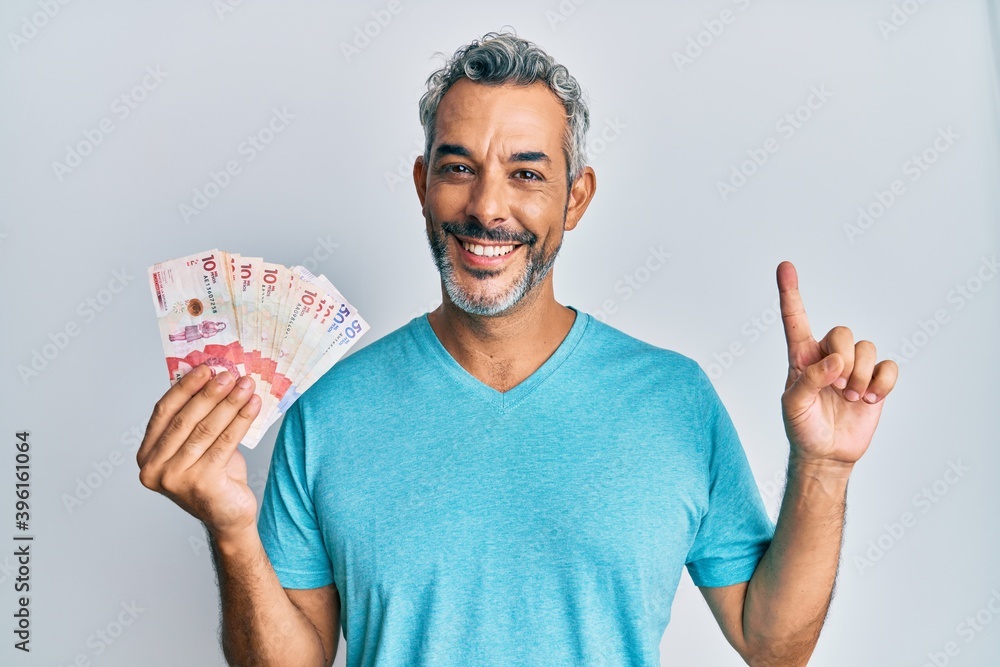 Middle age grey-haired man holding colombian pesos smiling with an idea or question pointing finger with happy face, number one Middle age grey-haired man holding colombian pesos smiling with an idea or question pointing finger with happy face, number one