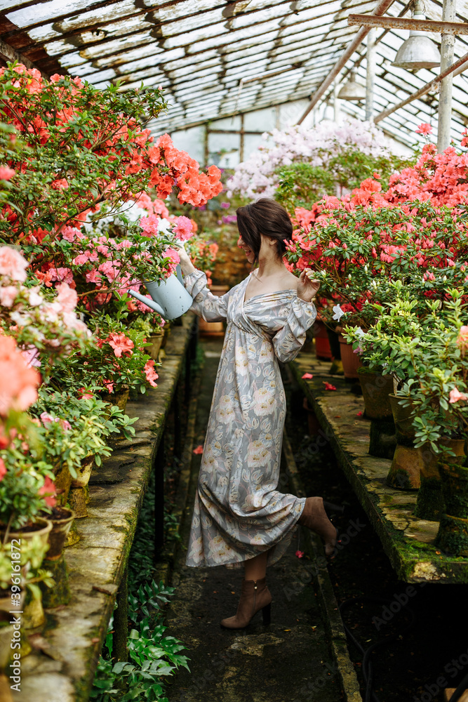 girl in a long dress in flowers with a watering can