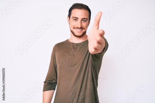 Young handsome man wearing casual clothes smiling friendly offering handshake as greeting and welcoming. successful business.