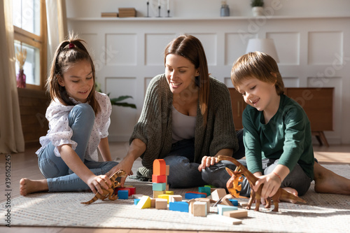 Caring single mother have fun play toys with excited two small kids at home. Happy loving young Caucasian mom engaged in game activity together with little children, enjoy family weekend indoors.