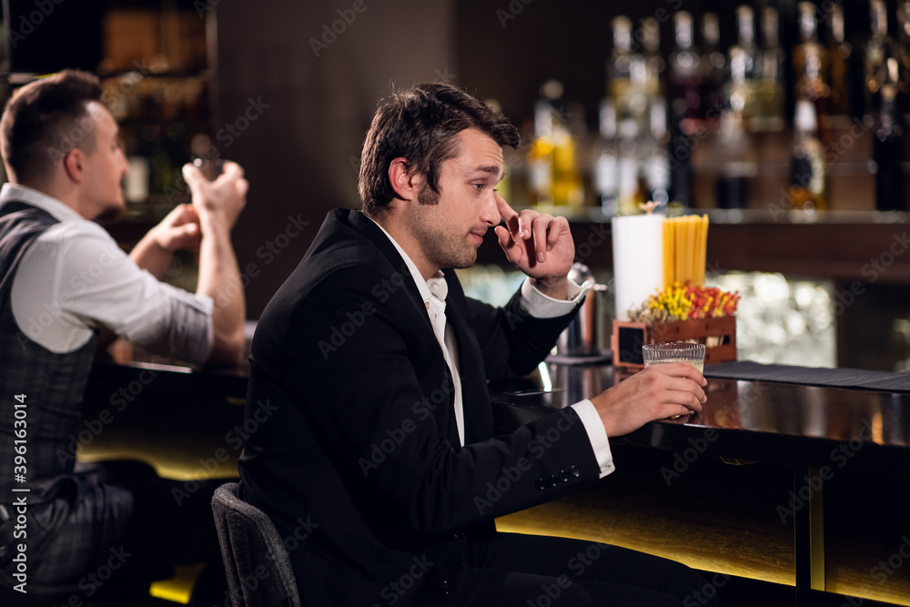 a young man drinks a cocktail at the bar, communicates with the bartender.