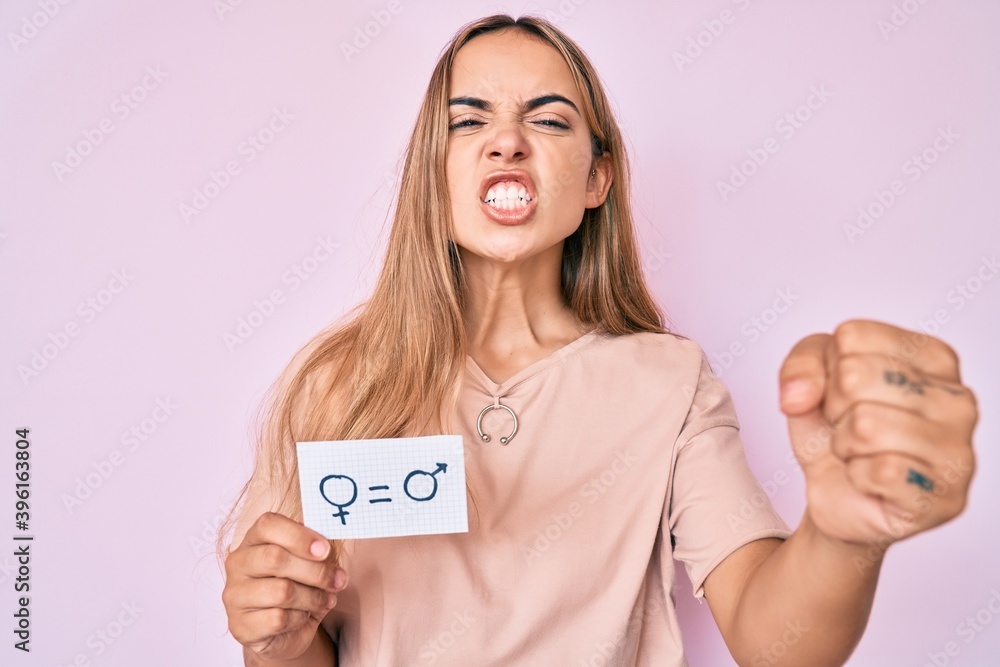 Young beautiful blonde woman holding we are equal paper annoyed and frustrated shouting with anger, yelling crazy with anger and hand raised Young beautiful blonde woman holding we are equal paper annoyed and frustrated shouting with anger, yelling crazy with anger and hand raised