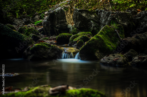 Mountain Stream flowing on the old stones with bright green moss and lichen in the wild forest. Clean water.