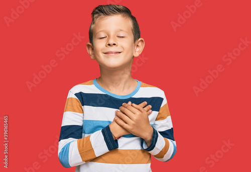 Adorable caucasian kid wearing casual clothes smiling with hands on chest with closed eyes and grateful gesture on face. health concept.