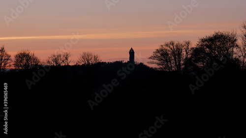 Orange evening sky above contrasty silhouette of the Wallace Monument tower on a hill in Stirling