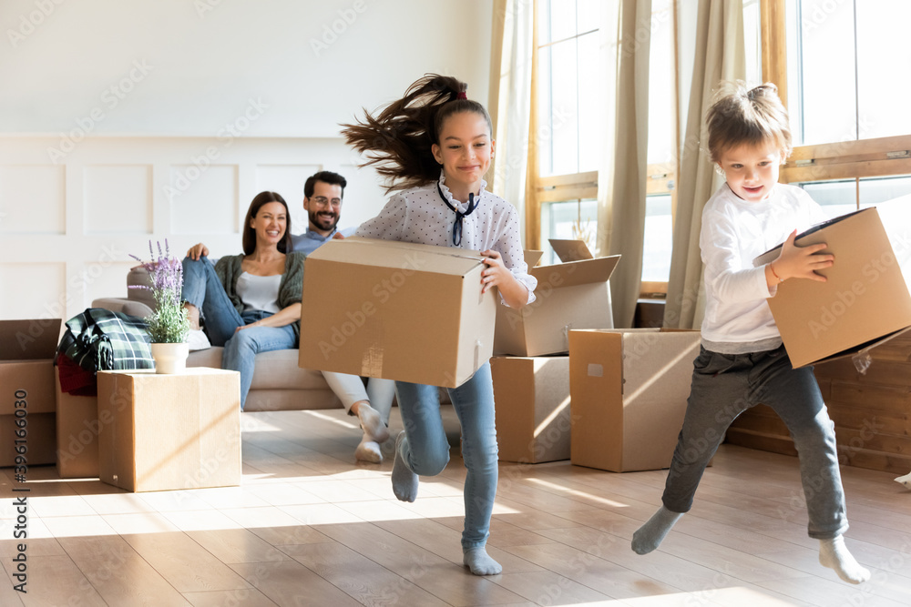 Happy little kids have fun carry unpack boxes moving in to new home with parents. Excited children unbox packages celebrate relocation to own house. Family relocation, real estate, rental concept. Happy little kids have fun carry unpack boxes moving in to new home with parents. Excited children unbox packages celebrate relocation to own house. Family relocation, real estate, rental concept.