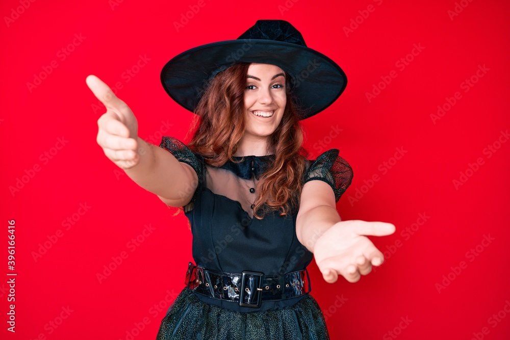 Young beautiful woman wearing witch halloween costume looking at the camera smiling with open arms for hug. cheerful expression embracing happiness. Young beautiful woman wearing witch halloween costume looking at the camera smiling with open arms for hug. cheerful expression embracing happiness.