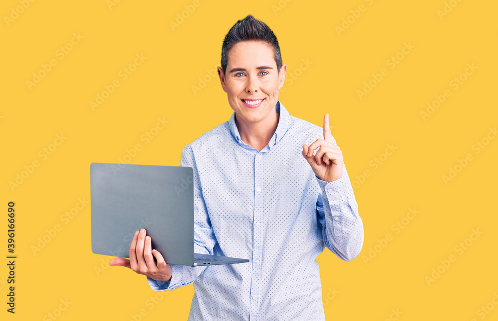 Young woman with short hair holding laptop surprised with an idea or question pointing finger with happy face, number one Young woman with short hair holding laptop surprised with an idea or question pointing finger with happy face, number one