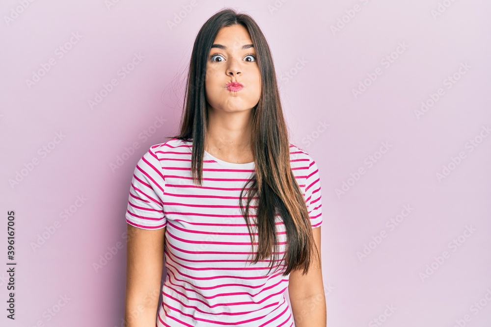 Young brunette woman wearing casual clothes over pink background puffing cheeks with funny face. mouth inflated with air, crazy expression. Young brunette woman wearing casual clothes over pink background puffing cheeks with funny face. mouth inflated with air, crazy expression.