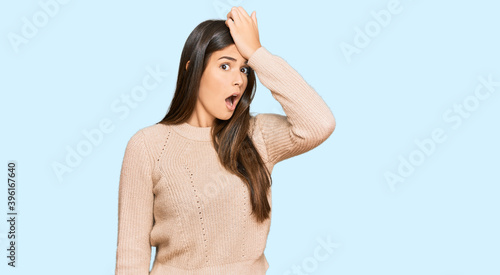 Young brunette woman wearing casual winter sweater surprised with hand on head for mistake, remember error. forgot, bad memory concept.