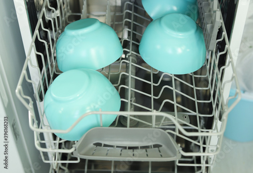 Blue deep plates in the dishwasher. Open dishwasher with clean plates. Selective focus.
