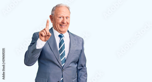 Senior handsome grey-haired man wearing elegant suit showing and pointing up with finger number one while smiling confident and happy.