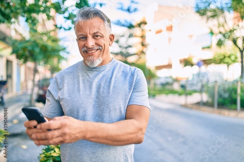 Middle age hispanic grey-haired man smiling happy using smartphone at the city.