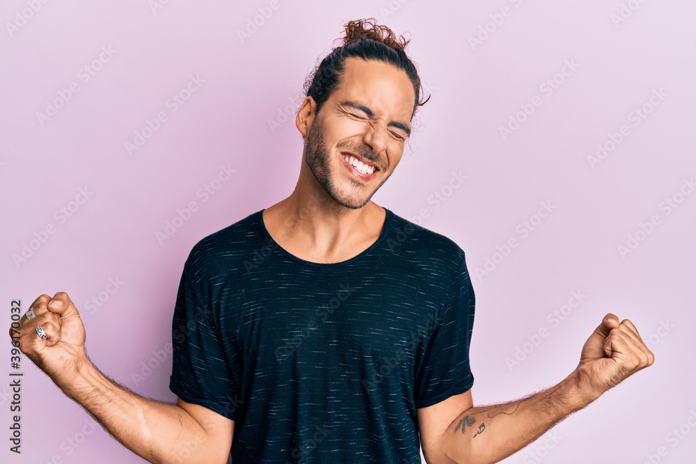 Young handsome man with long hair wearing casual clothes very happy and excited doing winner gesture with arms raised, smiling and screaming for success. celebration concept. Young handsome man with long hair wearing casual clothes very happy and excited doing winner gesture with arms raised, smiling and screaming for success. celebration concept.