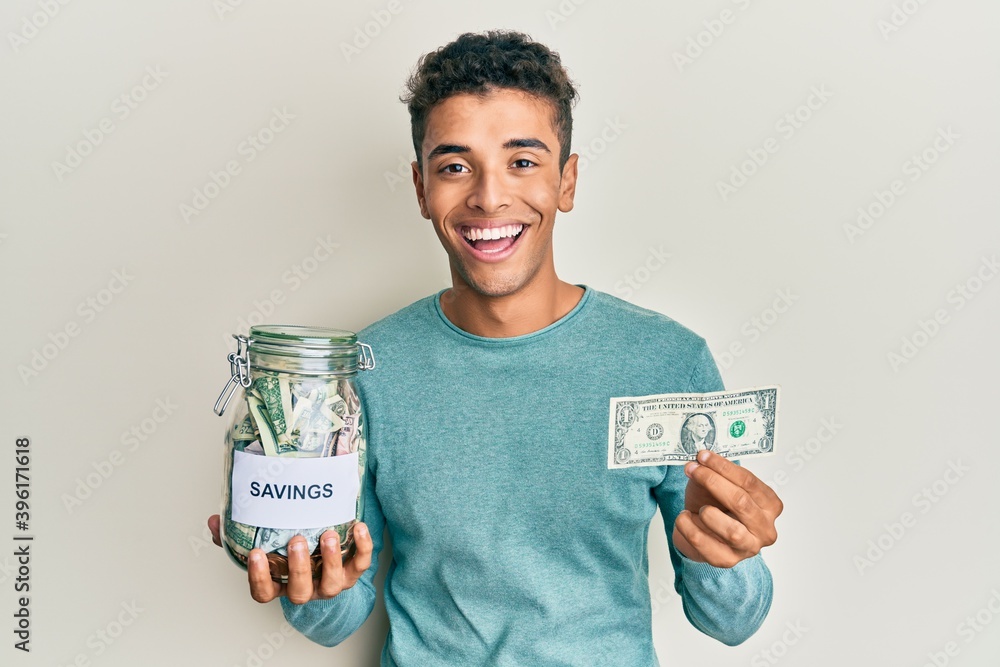 Young handsome african american man holding jar with savings smiling and laughing hard out loud because funny crazy joke. Young handsome african american man holding jar with savings smiling and laughing hard out loud because funny crazy joke.