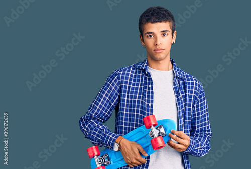 Young african amercian man holding skate thinking attitude and sober expression looking self confident photo