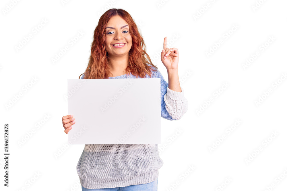 Young latin woman holding blank empty banner surprised with an idea or question pointing finger with happy face, number one Young latin woman holding blank empty banner surprised with an idea or question pointing finger with happy face, number one