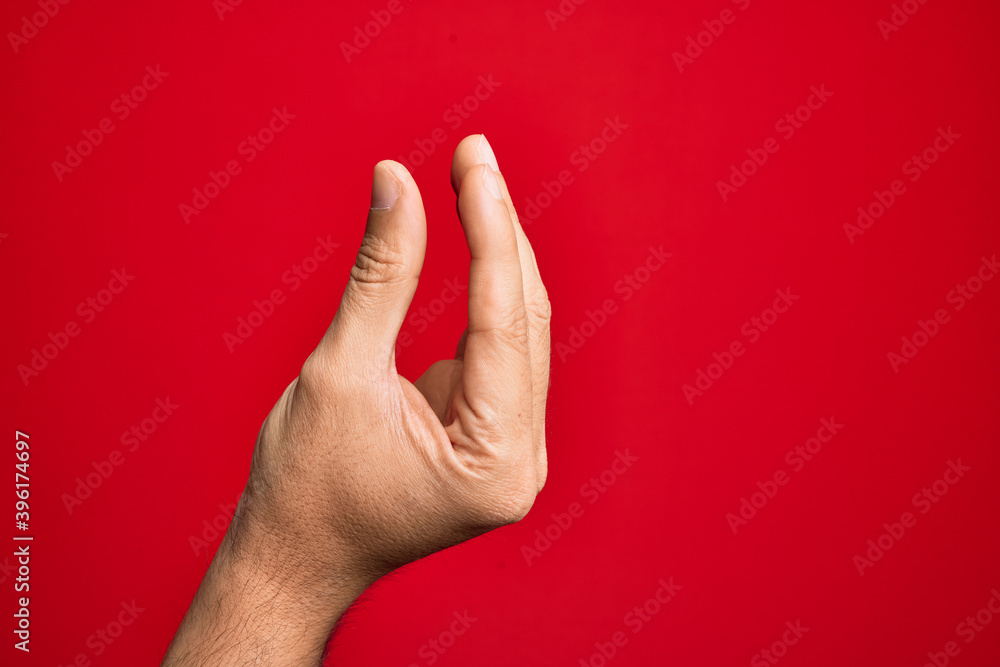 Hand of caucasian young man showing fingers over isolated red background picking and taking invisible thing, holding object with fingers showing space Hand of caucasian young man showing fingers over isolated red background picking and taking invisible thing, holding object with fingers showing space