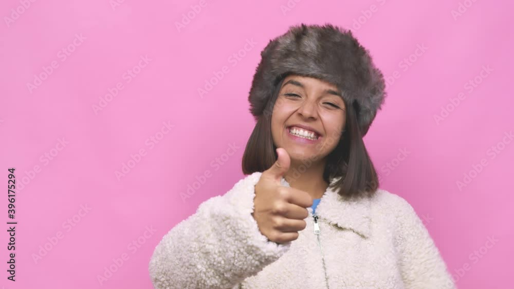Young hispanic woman wearing a winter hat face closeup smiling and raising thumb up Young hispanic woman wearing a winter hat face closeup smiling and raising thumb up