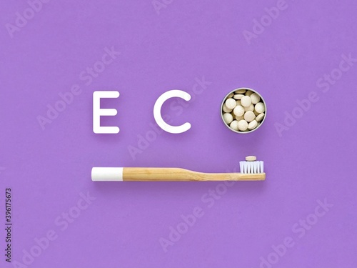 Bamboo toothbrush and toothpaste in tablets. Word Eco on a violet background. Plastic free, zero waste.