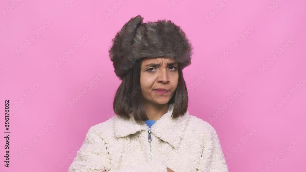 Young hispanic woman wearing a winter hat face closeup pointing with forefingers to a copy space, expressing excitement and desire Young hispanic woman wearing a winter hat face closeup pointing with forefingers to a copy space, expressing excitement and desire