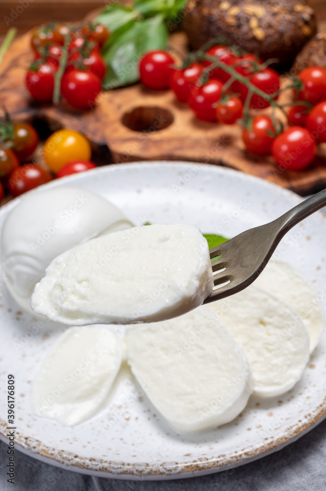 Cheese collection, eating. of white soft Italian cheese mozzarella, served with red cherry tomatoes, fresh basil leaves Cheese collection, eating. of white soft Italian cheese mozzarella, served with red cherry tomatoes, fresh basil leaves
