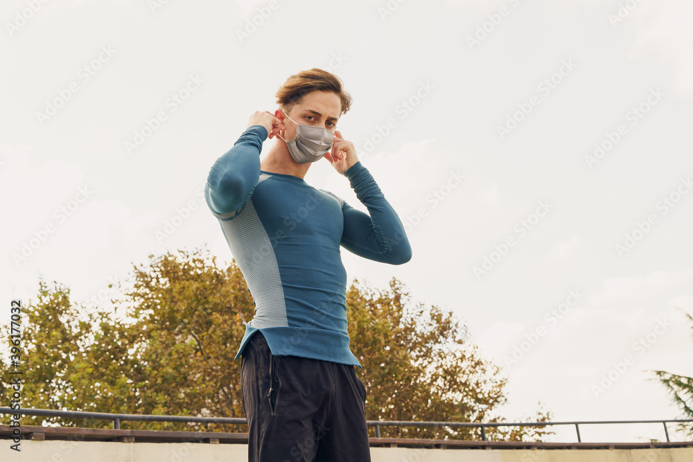 Athletic and handsome young male wearing a gray mask. Young athlete wearing a mask to train outside. Fit muscular sportsman dressed in sportswear wearing a gray mask.