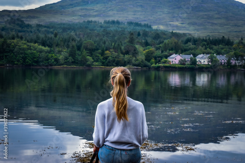 A woman meditating while sitting at the edge of a lake © Ben