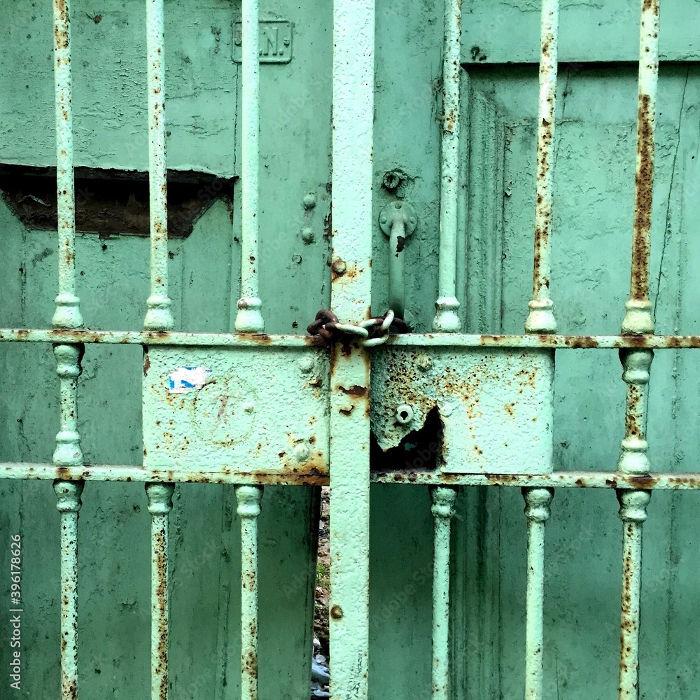 Detail of an old rusty iron and wood grid gate painted green closed with chain. Detail of an old rusty iron and wood grid gate painted green closed with chain.