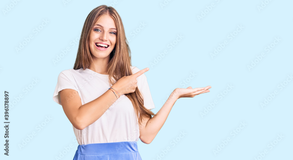 Young beautiful blonde woman wearing summer style amazed and smiling to the camera while presenting with hand and pointing with finger. Young beautiful blonde woman wearing summer style amazed and smiling to the camera while presenting with hand and pointing with finger.