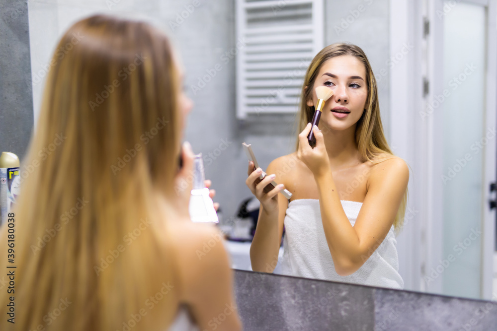 Portrait of attractive young woman applying blusher in her bathroom Portrait of attractive young woman applying blusher in her bathroom