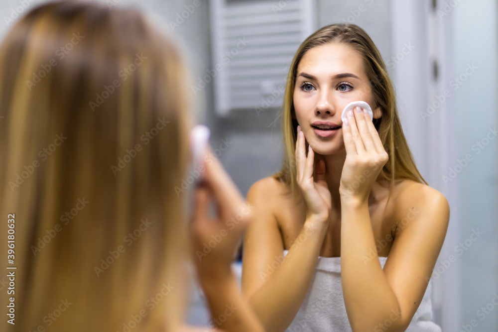 Young pretty woman is removing makeup with a cotton pad