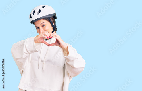 Beautiful brunette young woman wearing bike helmet and sporty clothes smiling in love doing heart symbol shape with hands. romantic concept. © Krakenimages.com