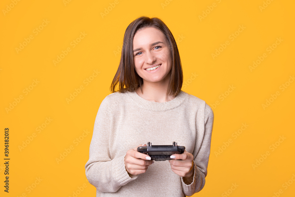 Portrait of smiling young woman using controller standing over yellow background. Portrait of smiling young woman using controller standing over yellow background.