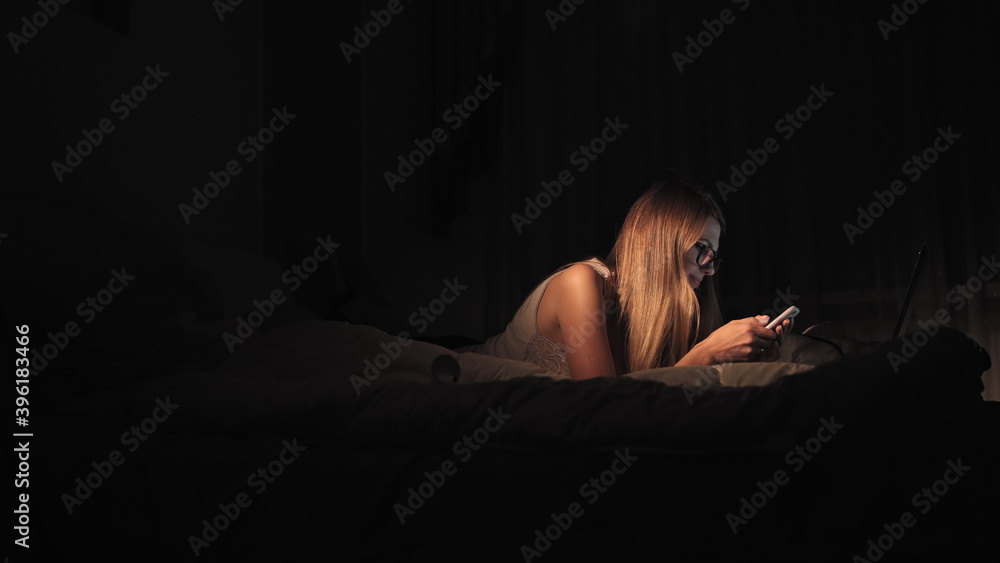 Happy girl selecting and watching video in a smart phone lying on the bed in the night at home