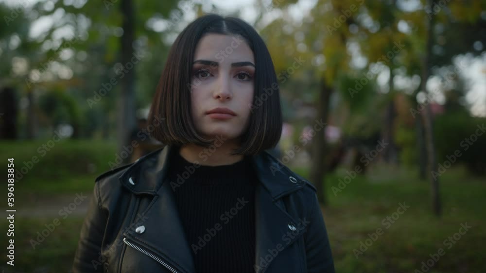 Portrait of a beautiful young woman standing in the park looking into the camera with a serious expression on her face Portrait of a beautiful young woman standing in the park looking into the camera with a serious expression on her face