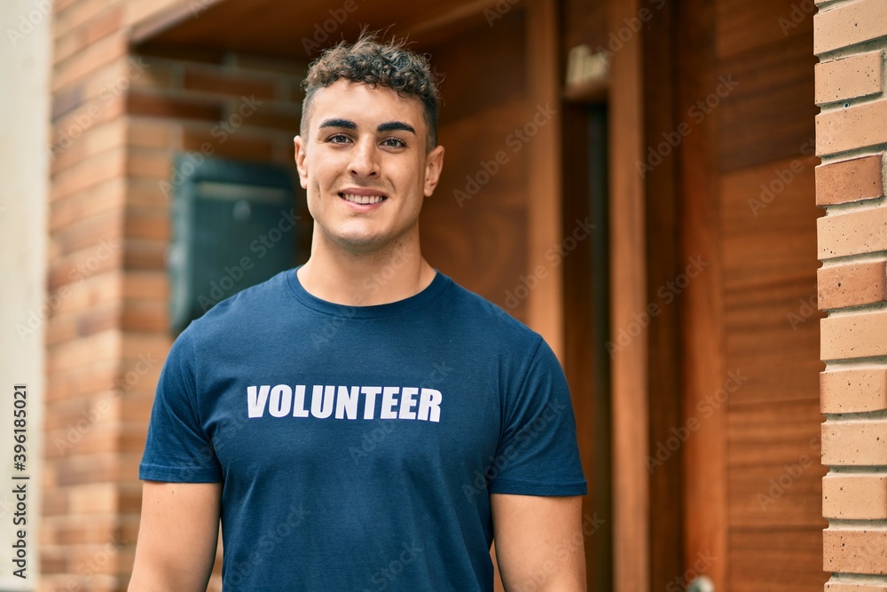 Obraz premium Young hispanic volunteer man smiling happy standing at the city.