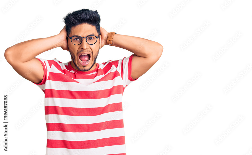 Handsome latin american young man wearing casual clothes and glasses crazy and scared with hands on head, afraid and surprised of shock with open mouth Handsome latin american young man wearing casual clothes and glasses crazy and scared with hands on head, afraid and surprised of shock with open mouth