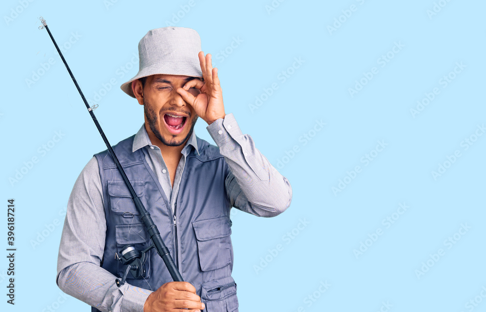 Handsome latin american young man wearing fisherman equipment smiling happy doing ok sign with hand on eye looking through fingers Handsome latin american young man wearing fisherman equipment smiling happy doing ok sign with hand on eye looking through fingers
