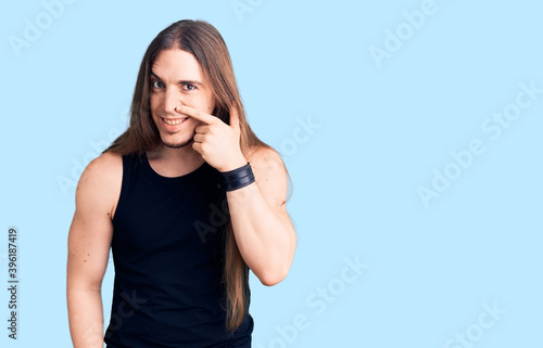 Young adult man with long hair wearing goth style with black clothes pointing with hand finger to face and nose, smiling cheerful. beauty concept © Krakenimages.com