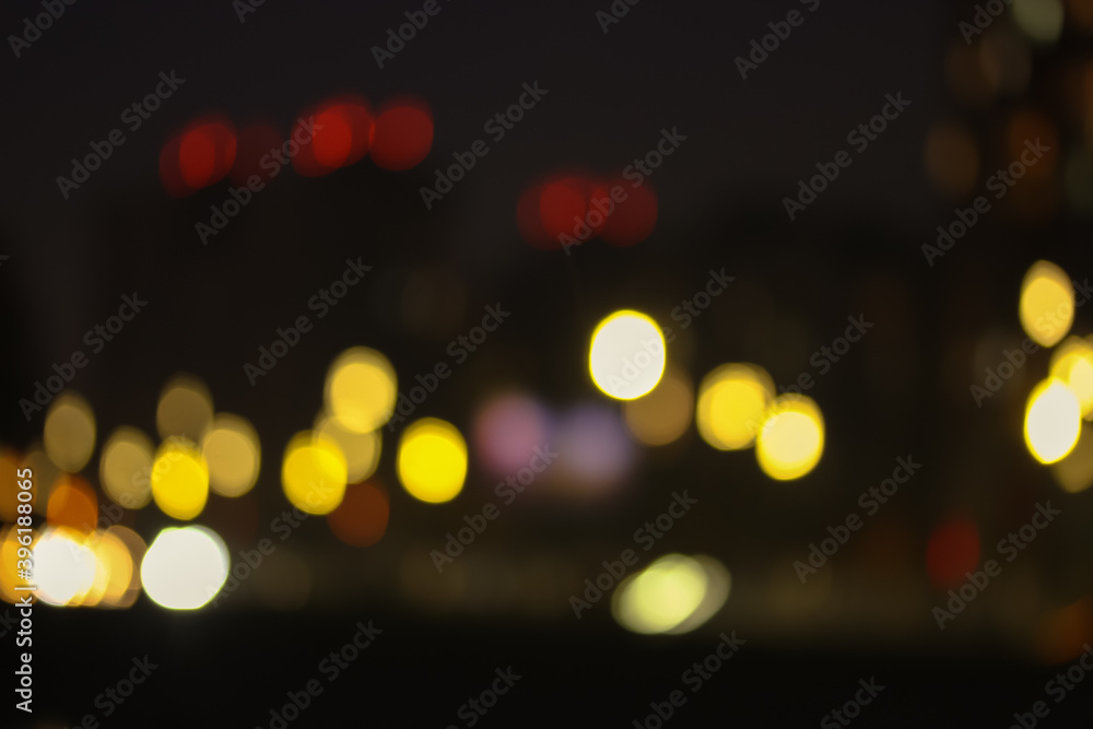 Fototapeta premium The facade of the apartment building, light in the windows in the evening, blurred houses in the big city and bright colorful abstract lights. 