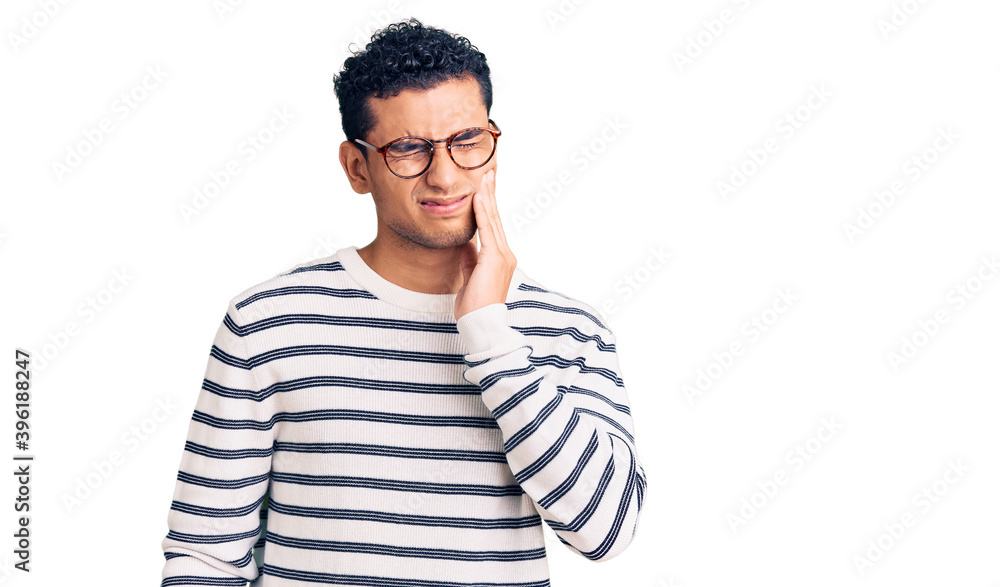 Hispanic handsome young man wearing casual clothes and glasses touching mouth with hand with painful expression because of toothache or dental illness on teeth. dentist Hispanic handsome young man wearing casual clothes and glasses touching mouth with hand with painful expression because of toothache or dental illness on teeth. dentist