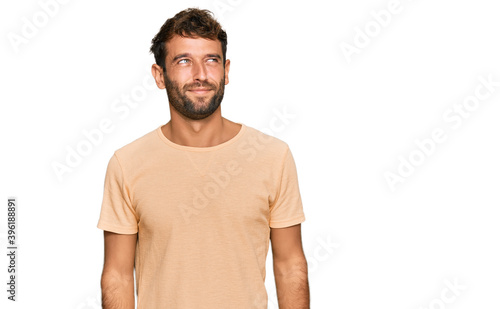 Handsome young man with beard wearing casual tshirt smiling looking to the side and staring away thinking. © Krakenimages.com