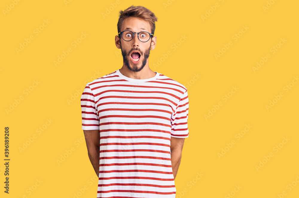 Handsome blond man with beard wearing casual clothes and glasses afraid and shocked with surprise and amazed expression, fear and excited face. Handsome blond man with beard wearing casual clothes and glasses afraid and shocked with surprise and amazed expression, fear and excited face.