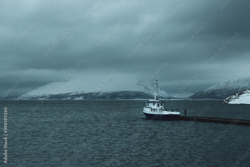 ship on pier in the sea in Norway Lyngen alps with snow covered mountains and dark clouds ship on pier in the sea in Norway Lyngen alps with snow covered mountains and dark clouds