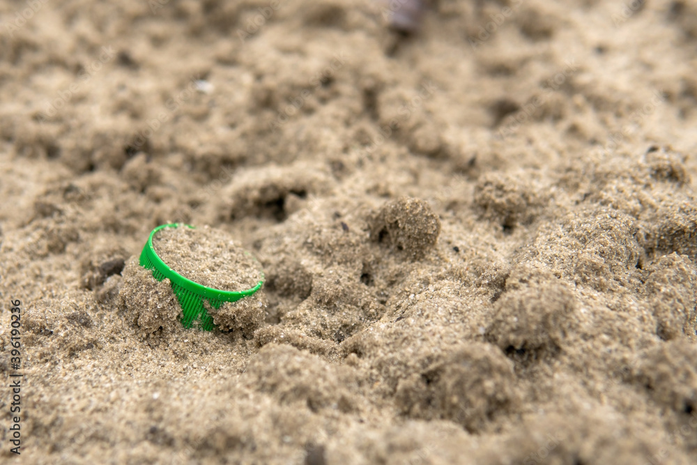 A green cork from a plastic bottle lies in the sand. Environmental pollution with plastic waste. Nature protection concept. Save ecology for future generations. A green cork from a plastic bottle lies in the sand. Environmental pollution with plastic waste. Nature protection concept. Save ecology for future generations.