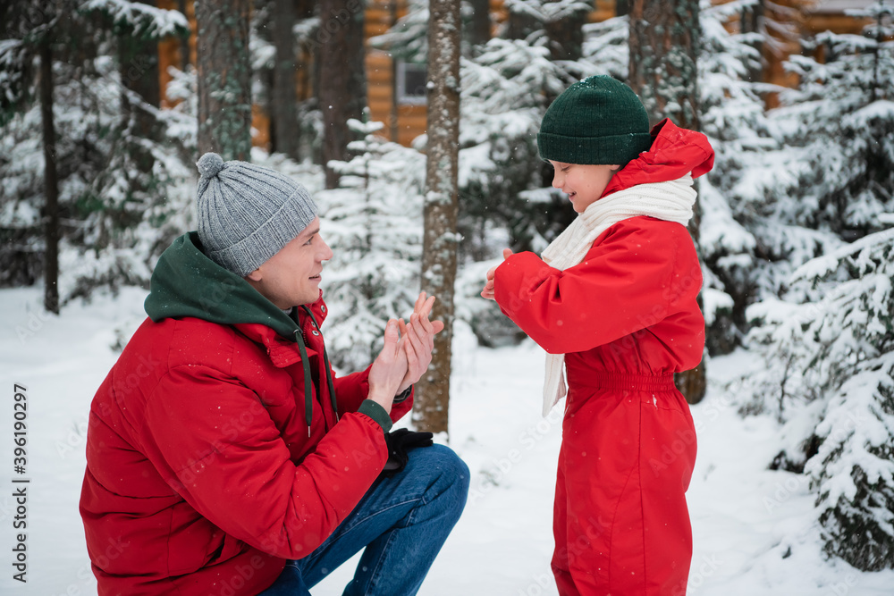 A young caring dad warms his son's hands on a cool winter day in the woods during a walk.