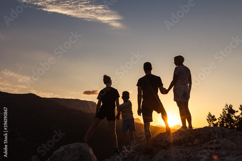 Happy family together in mountains at sunset holding hands looks into distance. Silhouettes of friendly people with children